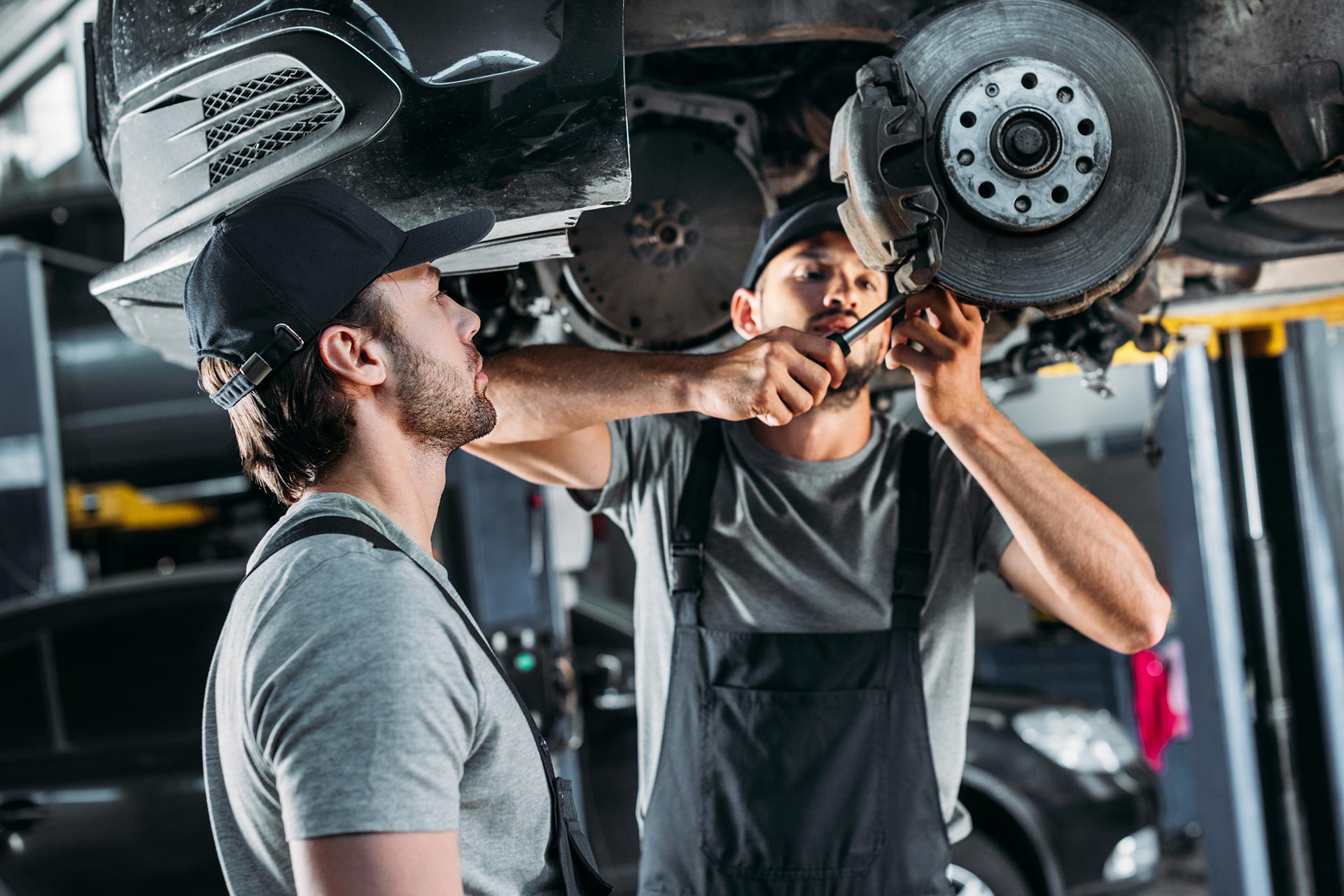 Two mechanics repairing a car in a well-equipped garage.